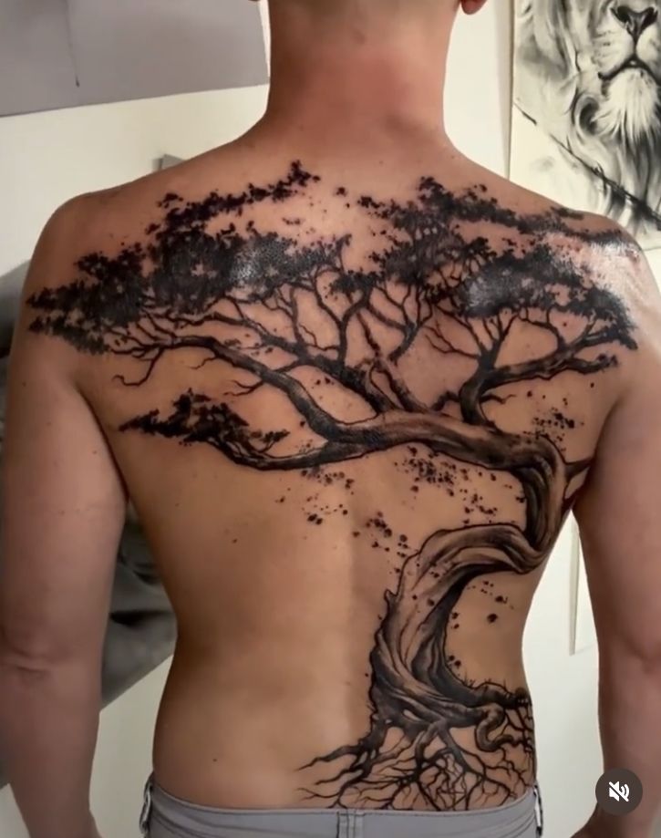 a man's back with a tree tattoo on his upper and lower part,