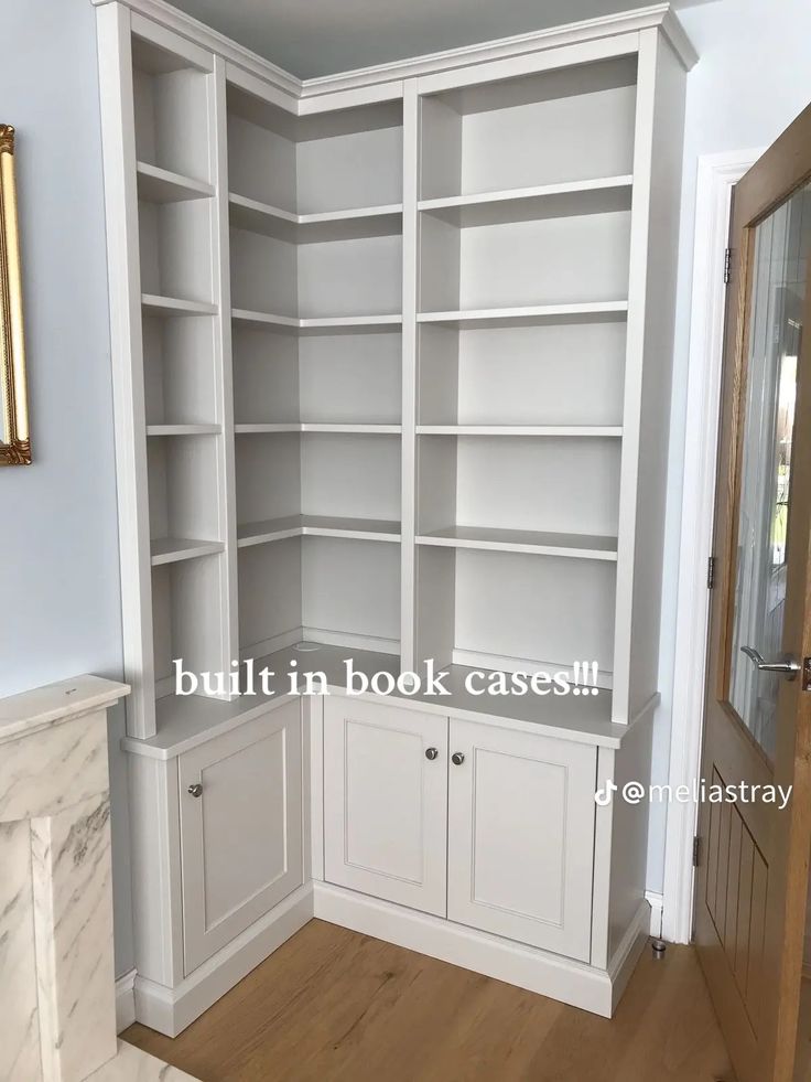 an empty white bookcase in the corner of a room with marble fireplace mantel