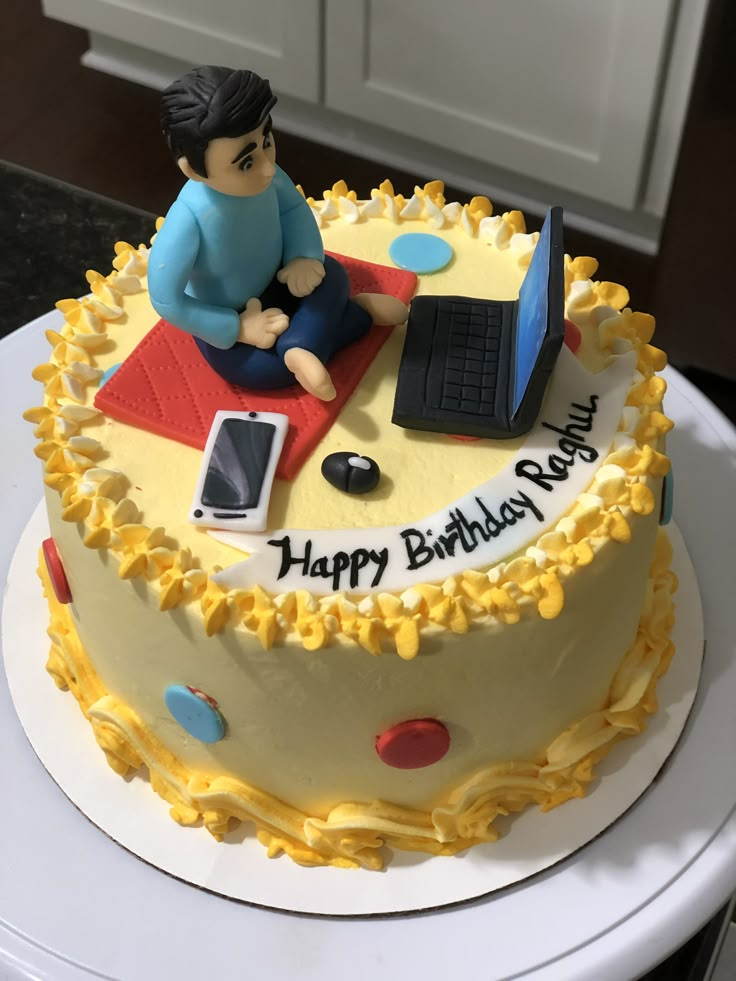 a birthday cake with a person sitting on the table using a laptop and cell phone