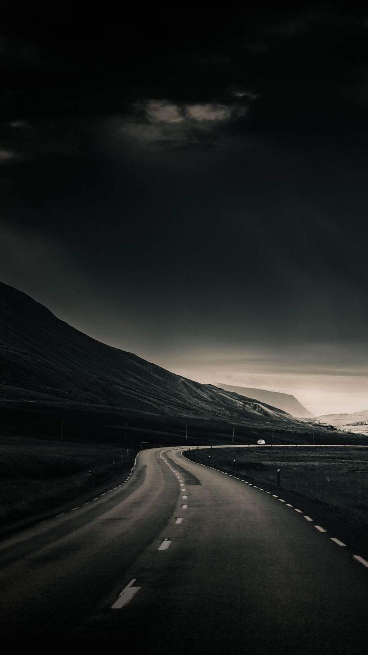 a black and white photo of an empty road in the middle of nowhere with dark clouds