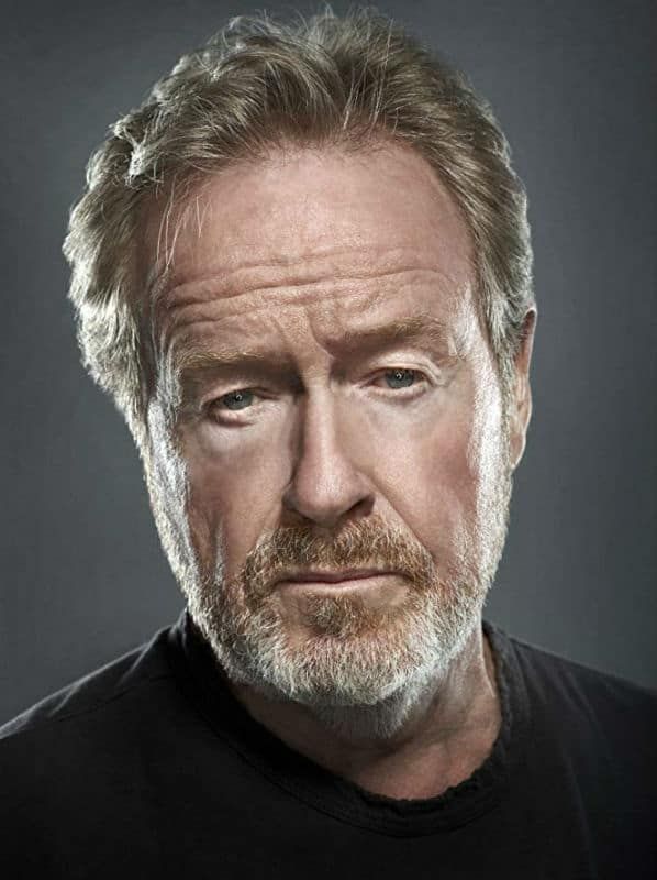 an older man with grey hair wearing a black t - shirt and looking at the camera