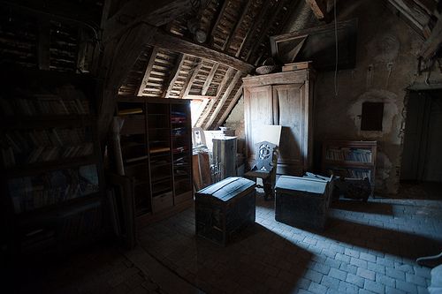 an old attic with furniture and bookshelves in the dark, lit by sunlight