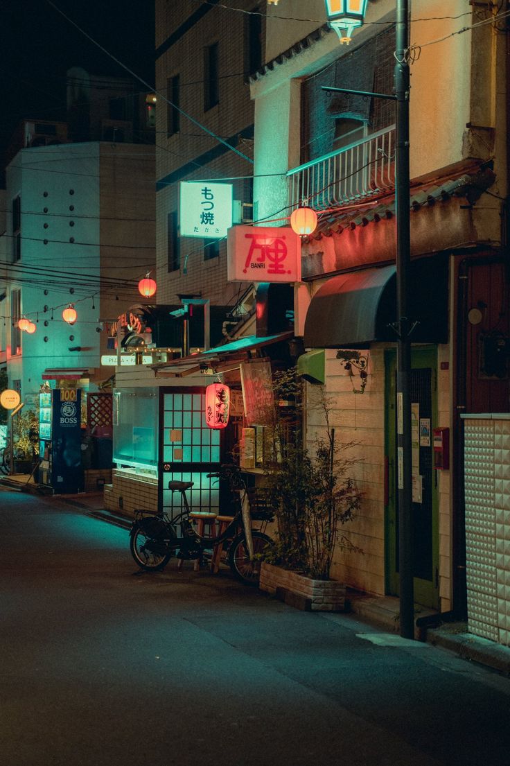 an empty street at night with neon lights on the buildings and bikes parked in front