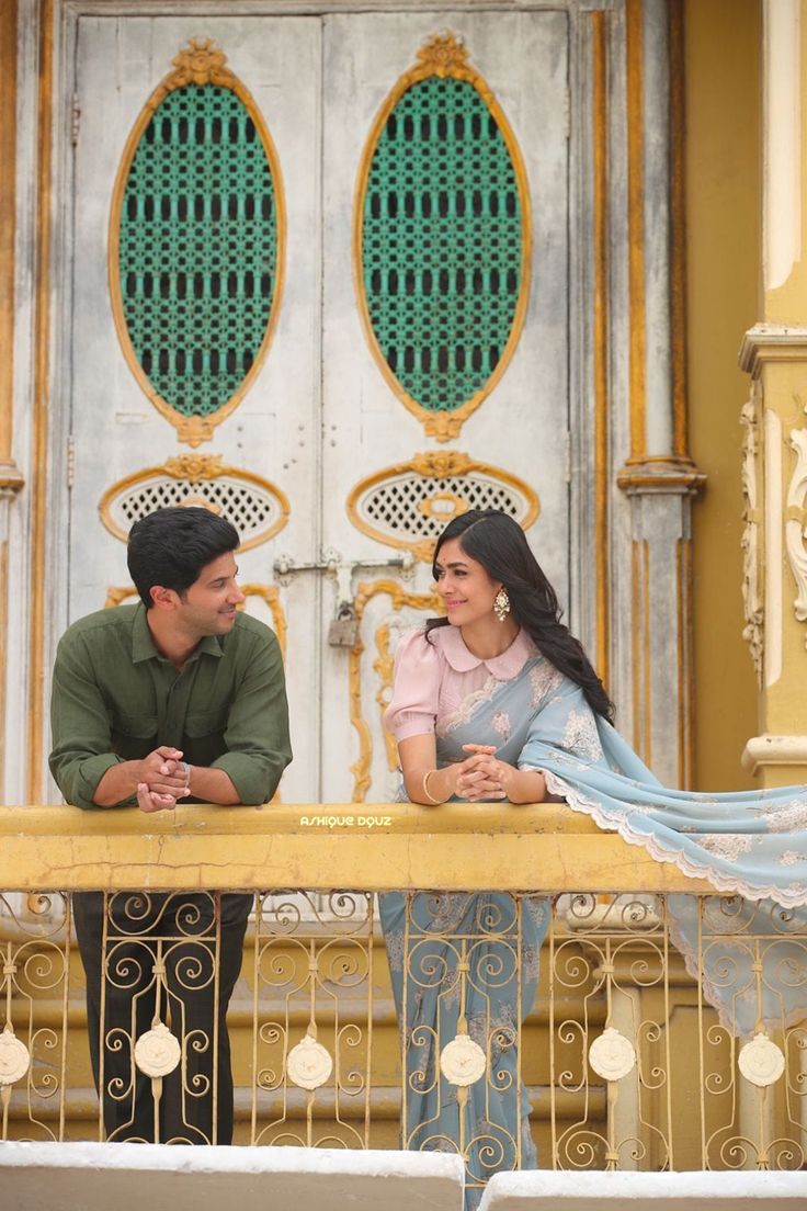 a man and woman sitting on a balcony looking into each other's eyes,