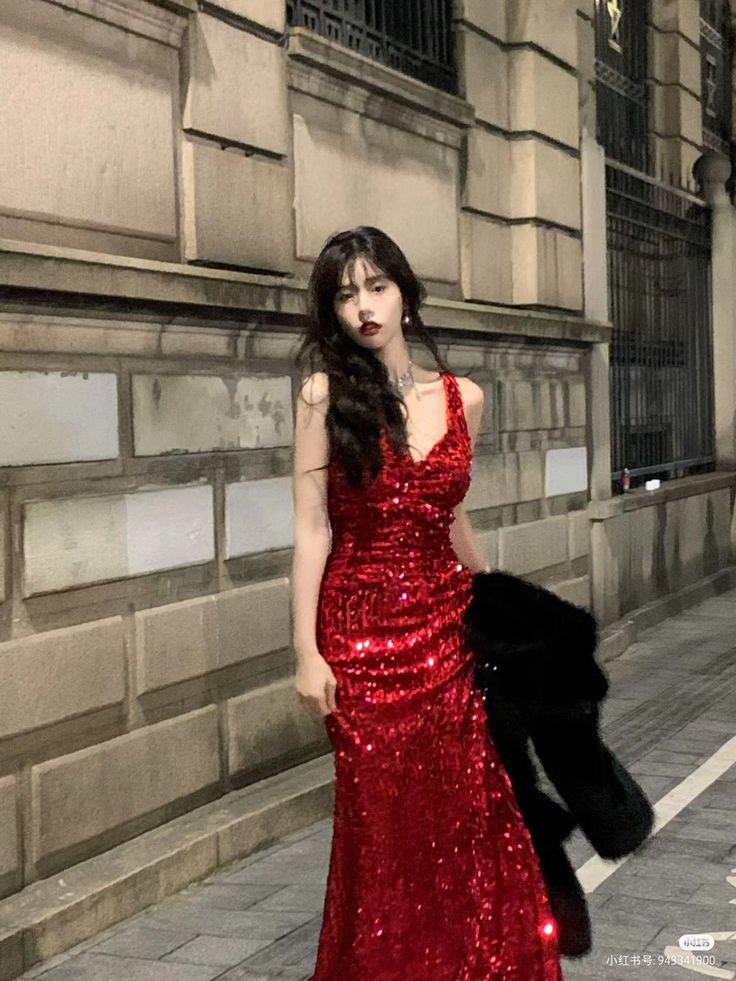 a woman in a red sequin dress standing on the sidewalk next to a building