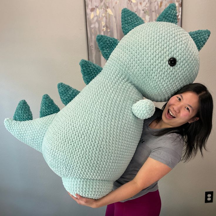 a woman is holding a large stuffed dinosaur