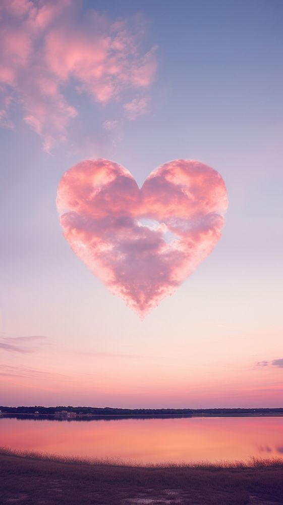 a heart shaped cloud floating in the sky over a body of water at sunset or dawn