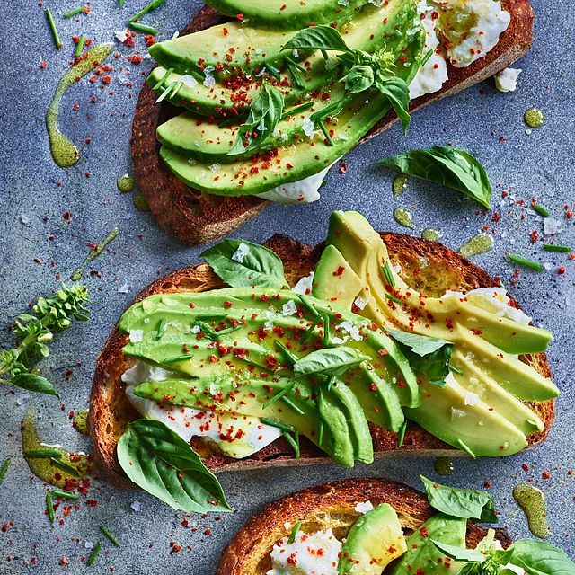 two pieces of bread topped with avocado and sour cream on a blue surface