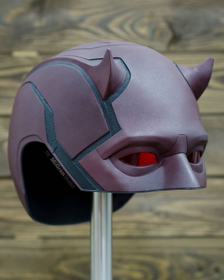 a purple helmet with red eyes and ears on a metal pole in front of a wooden wall