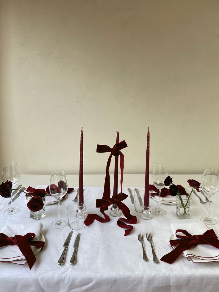 the table is set with silverware, wine glasses and red ribboned napkins