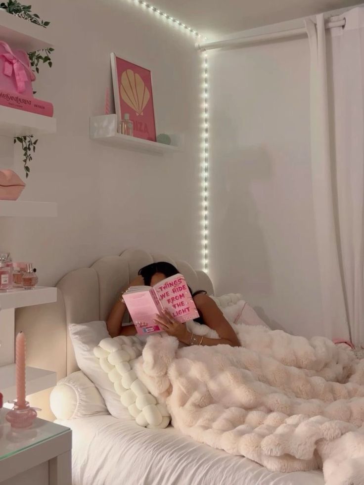 a woman laying on top of a bed with a book in her hand and lights above her head