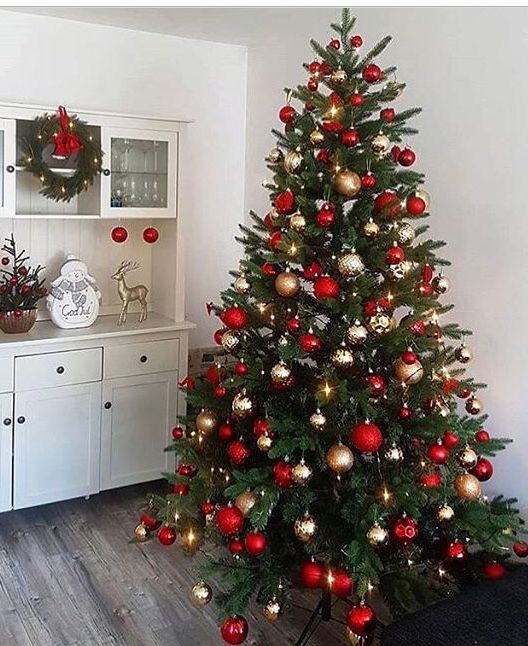 a decorated christmas tree with red and gold ornaments in a living room next to a white hutch