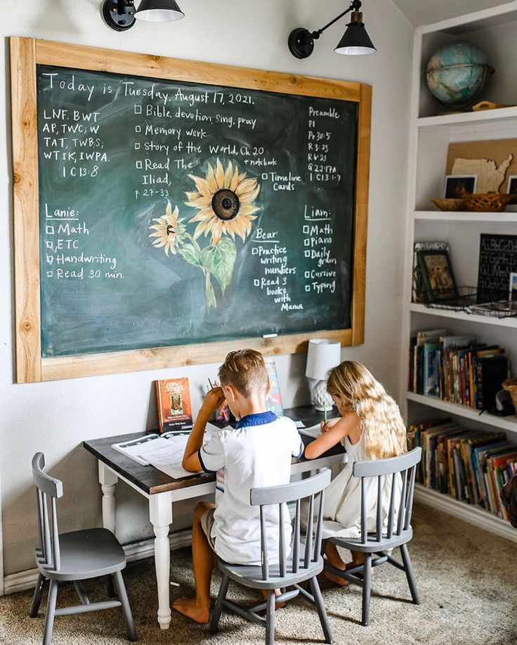 two children sitting at a table in front of a chalkboard