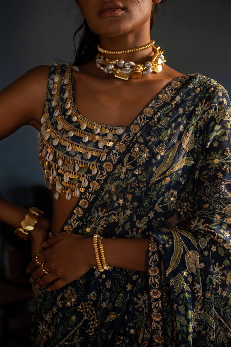 Editor's Note Presenting a stunning navy blue pre-draped sari, featuring our signature print and antique tone marodi work borders. The sari showcases a highlighted pallu, adding an exquisite touch. Paired with a cotton silk base blouse, heavily embellished with kowri shells and golden tone sequins, the ensemble exudes opulence and elegance. Complete with our signature belt, this sari set is a true embodiment of style. Step into any occasion with confidence, draped in this captivating navy blue p Shell Work Blouse, Desi Suits, Marodi Work, Paulmi And Harsh, Brown Barbie, Fashion Education, Shell Blouse, Blouse Sari, Haldi Outfits