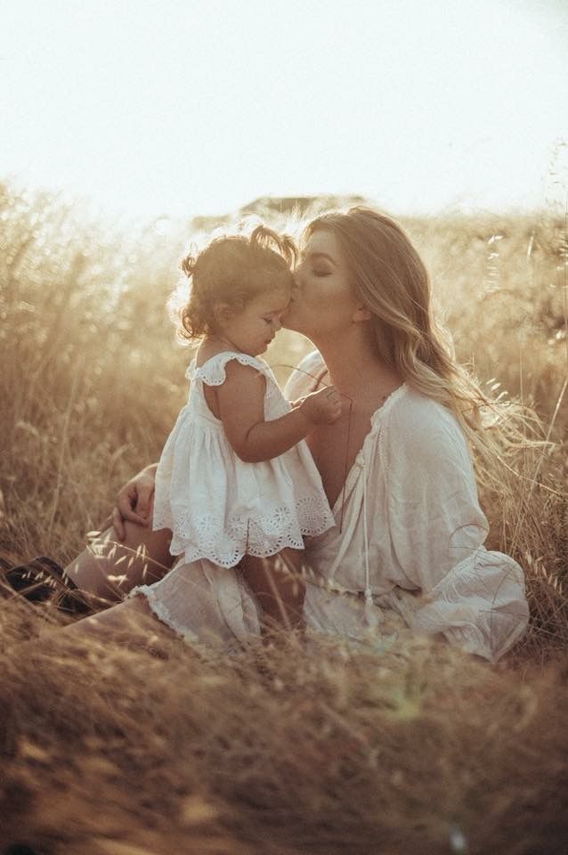 a woman holding a small child in her lap while sitting on the ground with tall grass