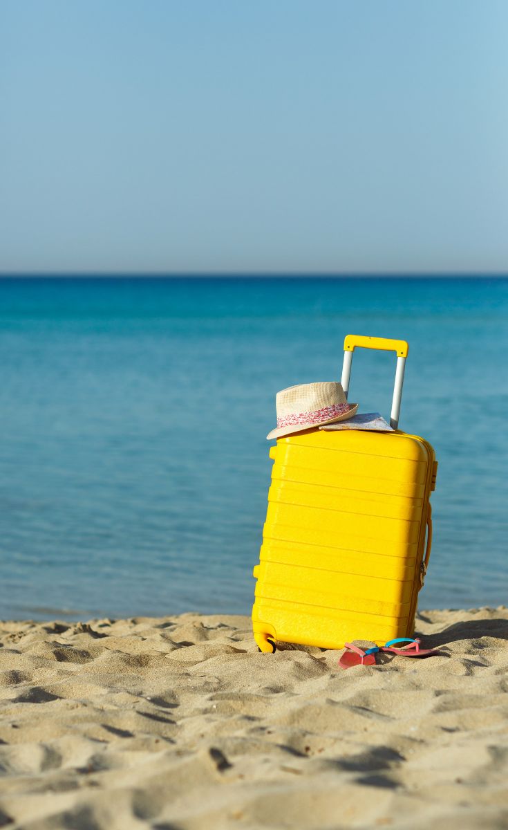 a yellow piece of luggage sitting on top of a sandy beach next to the ocean