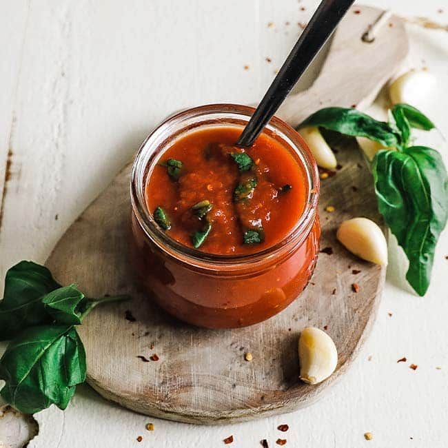 a glass jar filled with sauce and garnished with basil on a cutting board