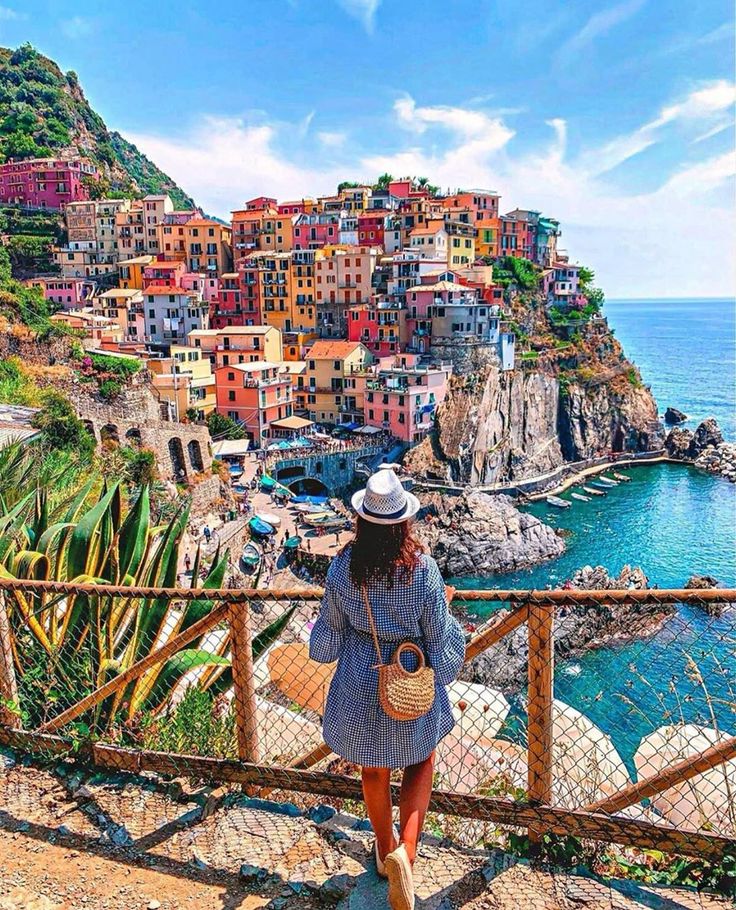 a woman in a hat is looking at the ocean and buildings on the cliff side