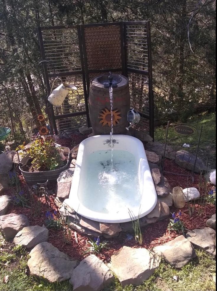 an outdoor bathtub in the middle of some rocks and plants with water coming out of it