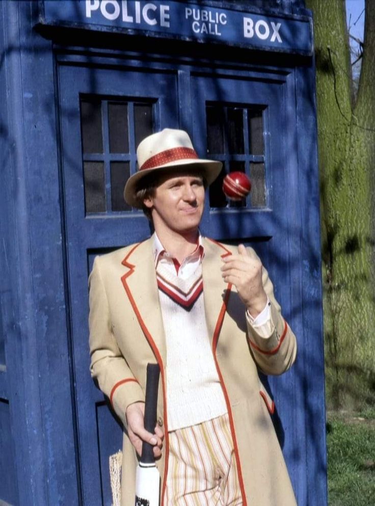 a man dressed as a doctor who is holding an apple in front of a police box