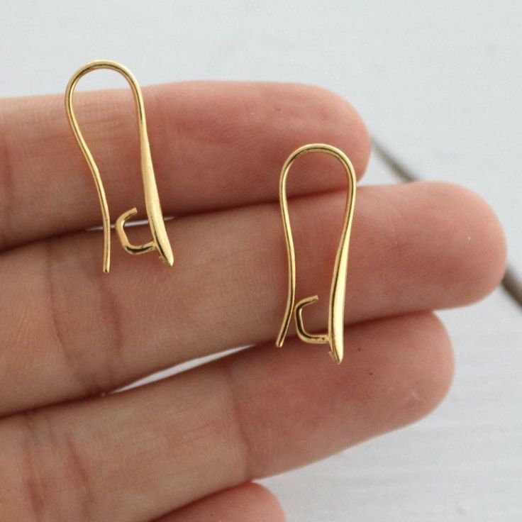 a pair of small gold earrings sitting on top of a person's hand