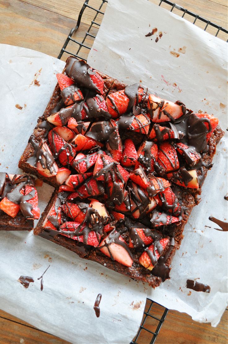 a chocolate dessert with strawberries and chocolate drizzled on top is sitting on a cooling rack