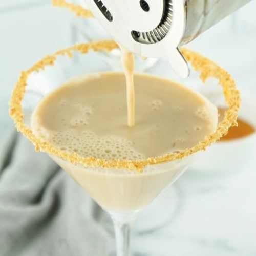 someone pouring something into a martini glass with an orange and white straw garnish