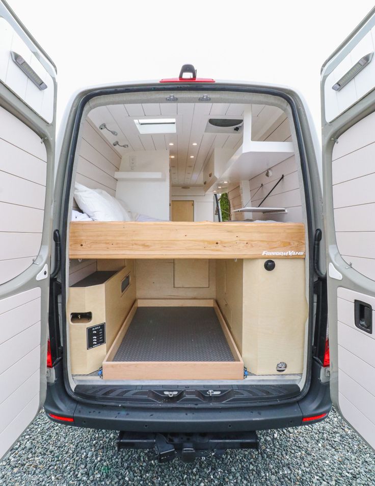 the back end of a van with its door open and storage compartments opened on gravel ground