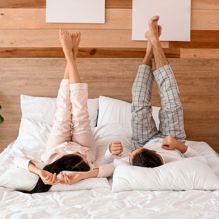 two people laying on a bed with their arms in the air