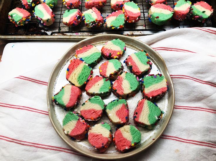 a plate full of colorful cookies sitting on top of a table next to a cooling rack