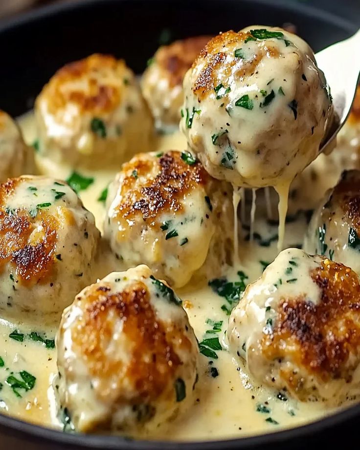 a ladle full of cheese covered meatballs being held by a wooden spatula