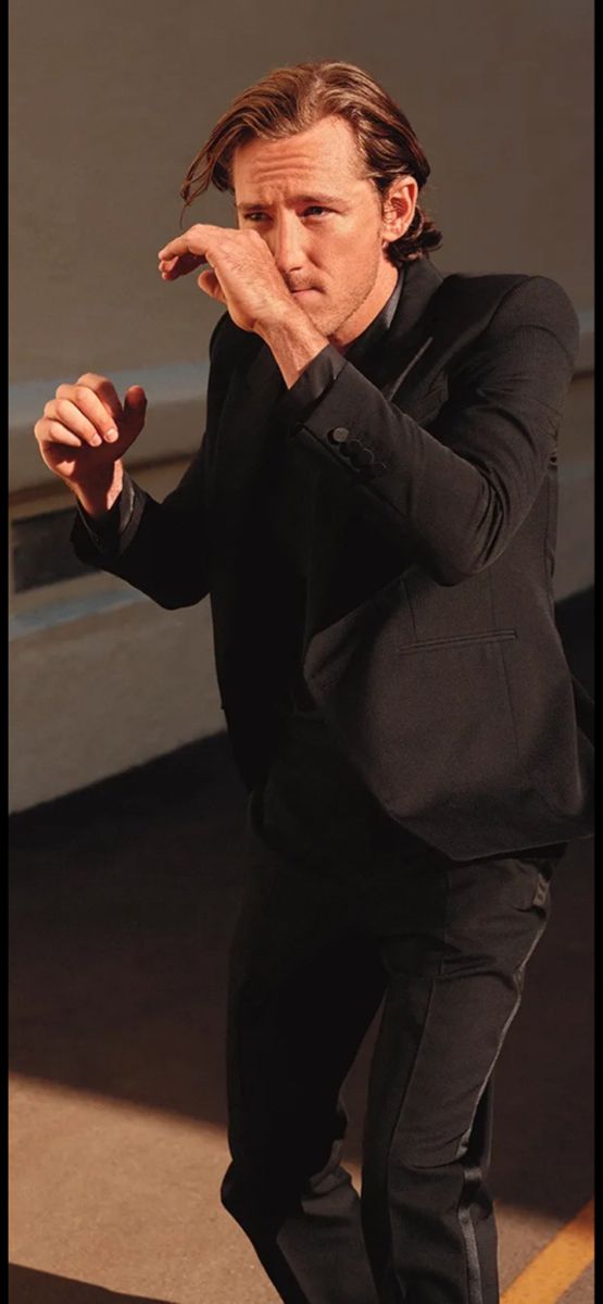 a man in a black suit is holding his hand to his face and pointing at something