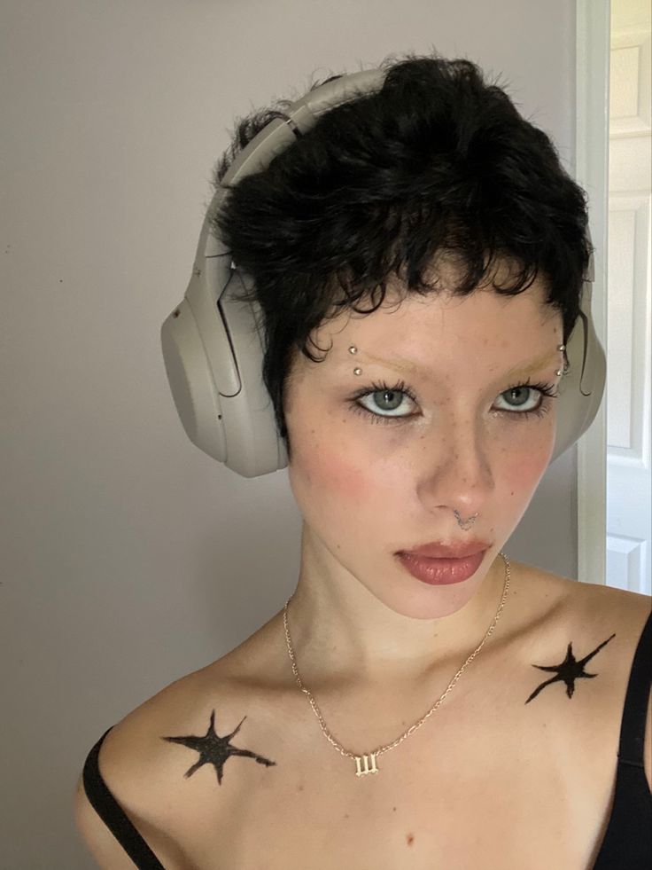 a woman with headphones on her ears and stars painted on her chest is looking at the camera