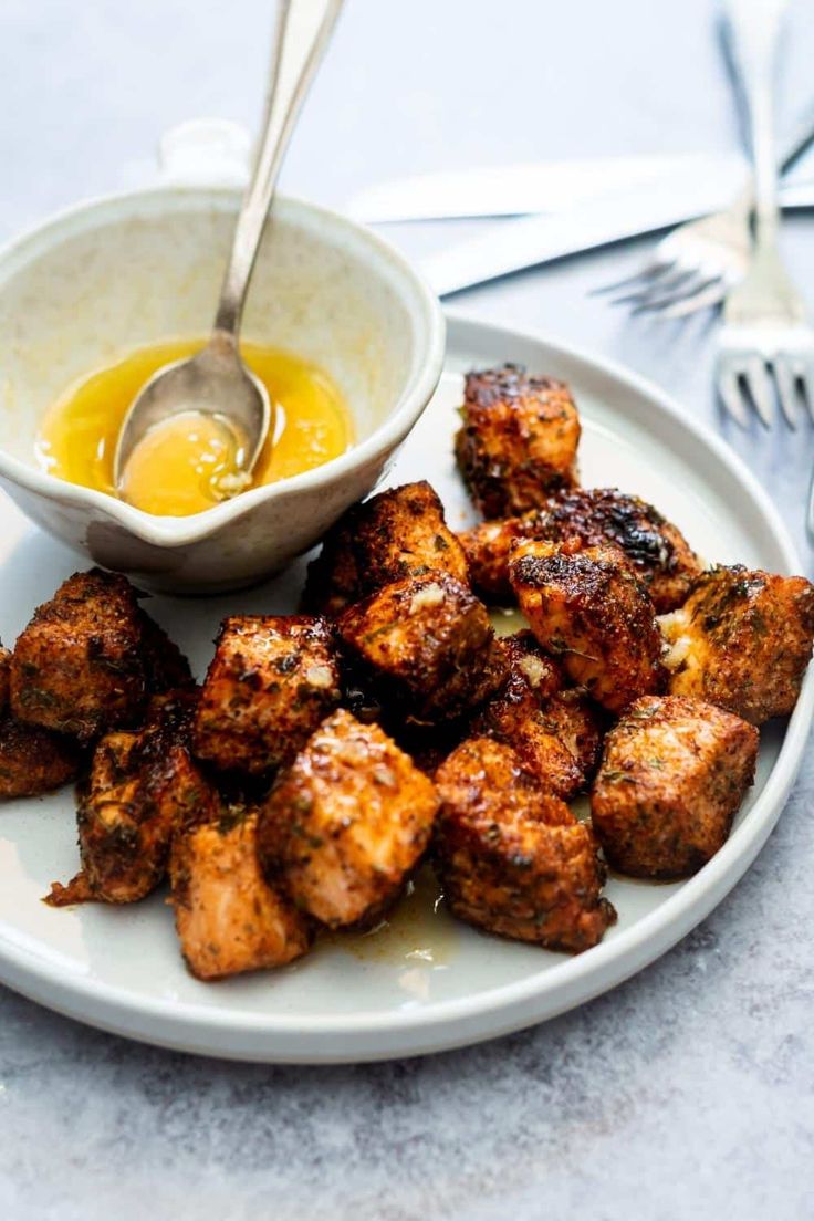 a white plate topped with fried food next to a bowl of sauce