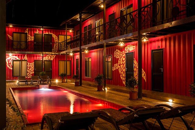 an empty pool in front of a red building with lights on it and two lawn chairs next to the pool