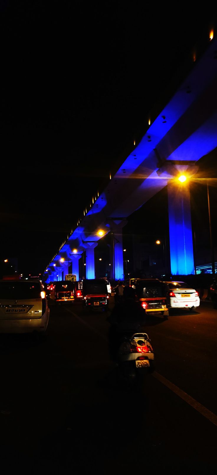 many cars are driving on the road at night time with blue lights in the background