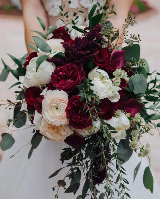 a bridal holding a bouquet of red and white flowers with greenery on it