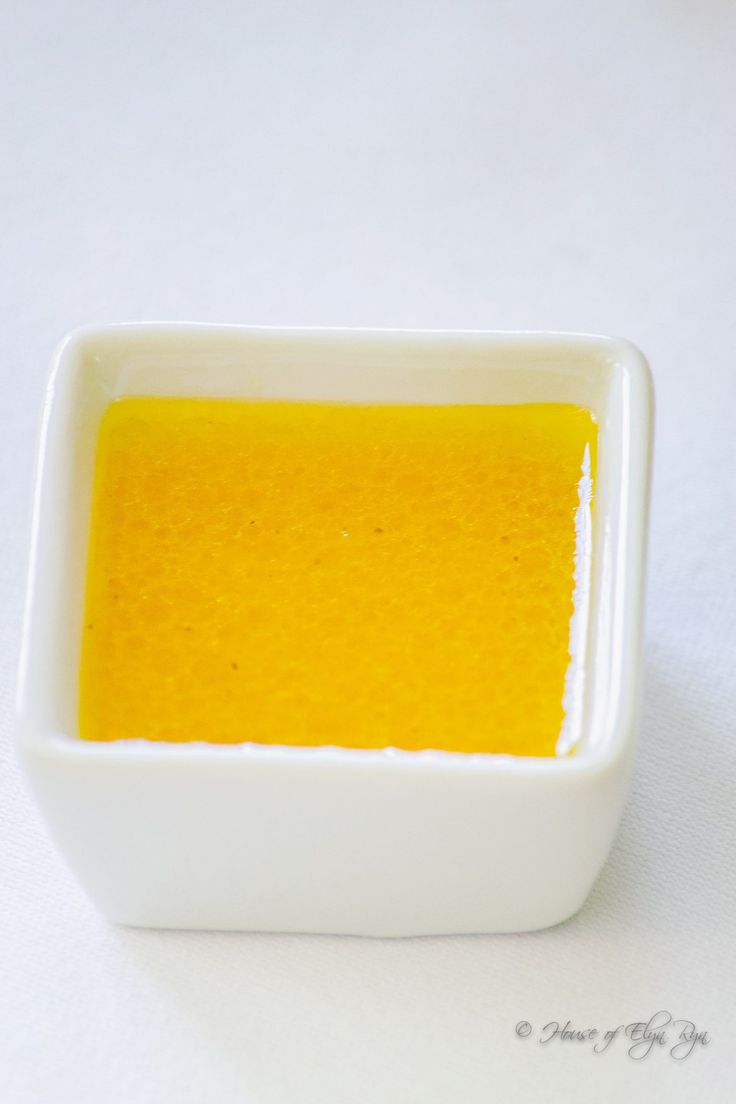 a small white bowl filled with yellow liquid on top of a white tableclothed surface