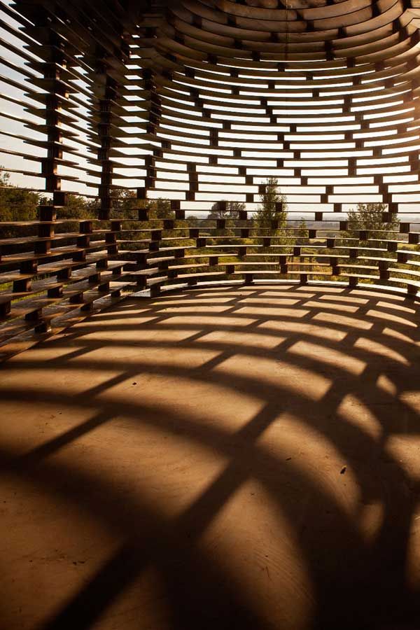 the sun shines through an abstract structure made out of wooden strips and sticks, with shadows on the ground