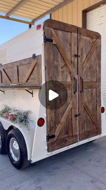 a horse trailer with wooden doors and flowers on the back door is parked in front of a building