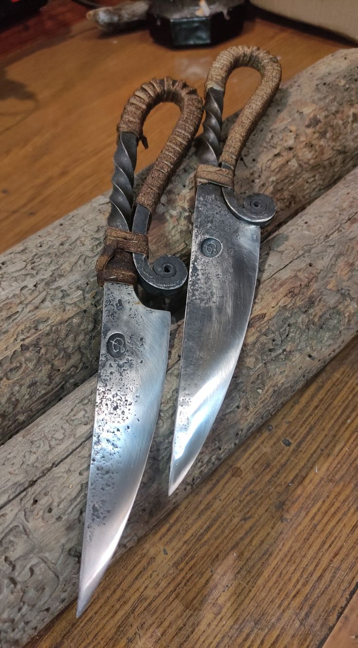 two knives are sitting on top of a piece of wood with rope wrapped around them