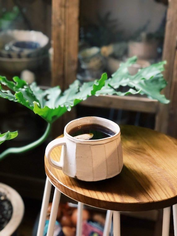 a wooden table topped with a cup of coffee next to a potted green plant