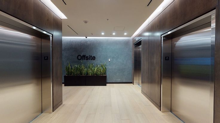 an office hallway with two elevators and plants on the wall in front of them that says offslie