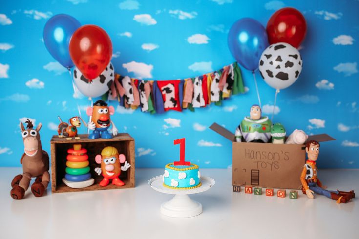 a birthday party with balloons, toys and decorations on a table in front of a blue wall