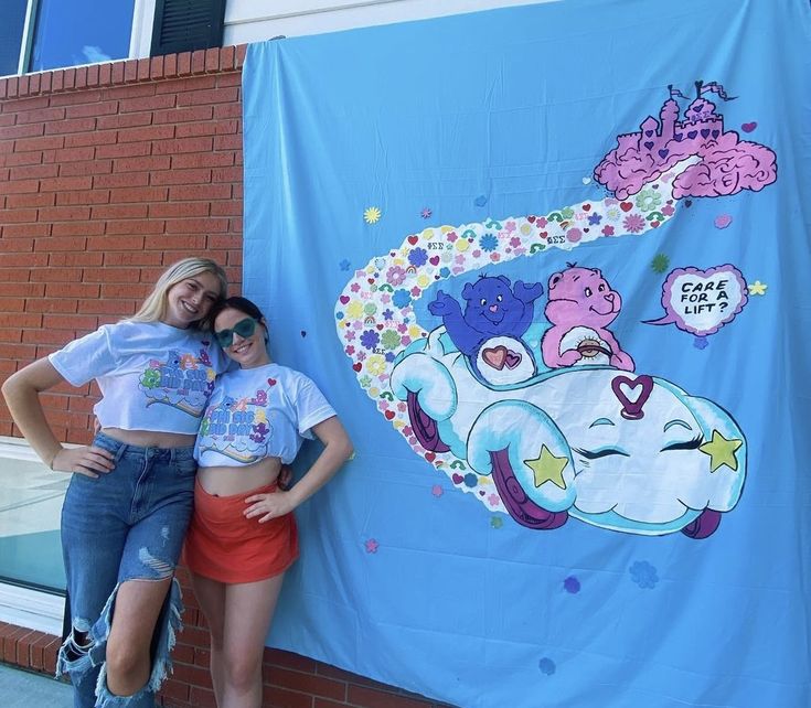 two young women standing next to a large blue banner on the side of a building