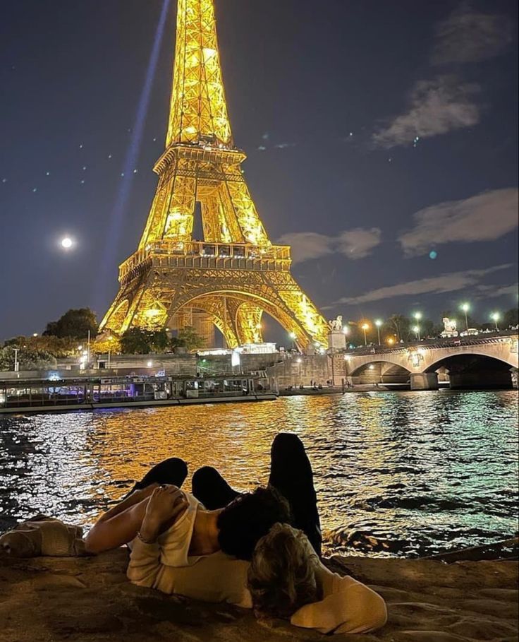 two people laying on the ground in front of the eiffel tower at night