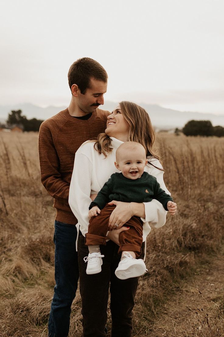 a man and woman holding a baby in their arms while standing in the middle of a field