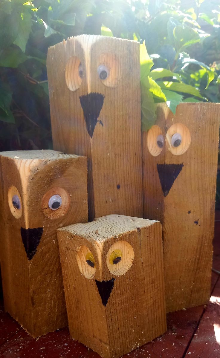 four wooden owls sitting on top of each other in front of some plants and bushes