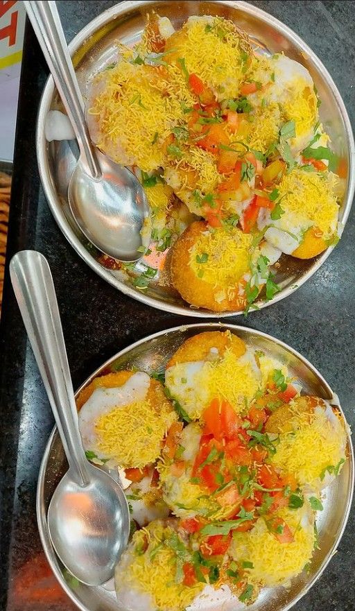 two silver plates with food on them and spoons next to each other in the same bowl