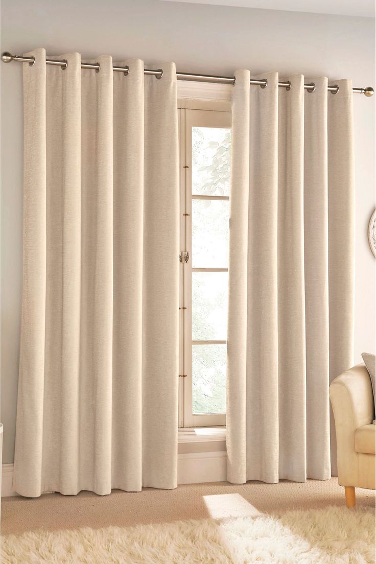 a living room with white curtains and a chair in front of a window that has a clock on the wall